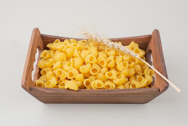 Uncooked pasta on wooden plate with colorful ear of wheat