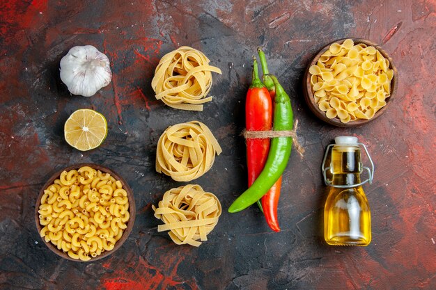 Uncooked pastas cayenne peppers tied in one another with rope oil bottle lemon garlic on mixed color table