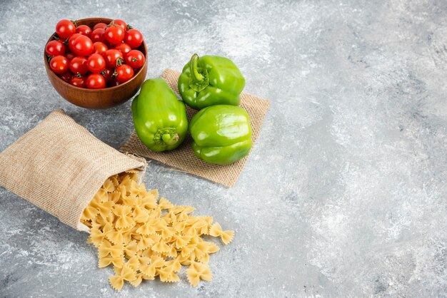 Pasta cruda in un sacchetto rustico con pomodorini e peperoni su tavola di marmo.