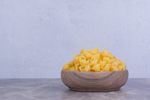 Uncooked pastas in a wooden plate isolated on the marble surface