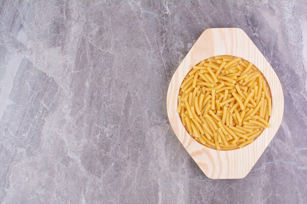 Uncooked pastas in a wooden plate isolated on the marble surface