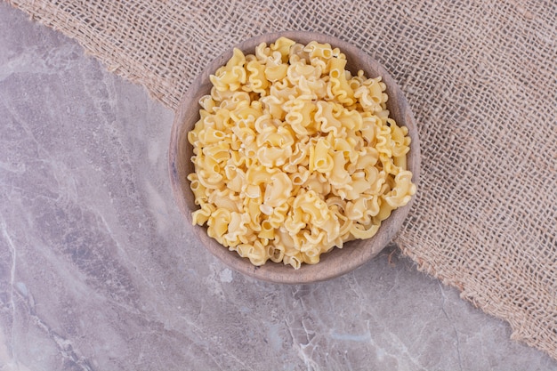 Free photo uncooked pastas in a wooden plate isolated on the marble surface