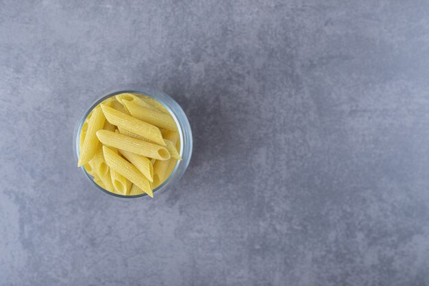 Uncooked penne pasta in glass on stone background. 