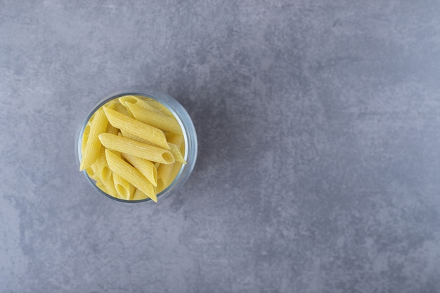 Uncooked penne pasta in glass on stone background. 