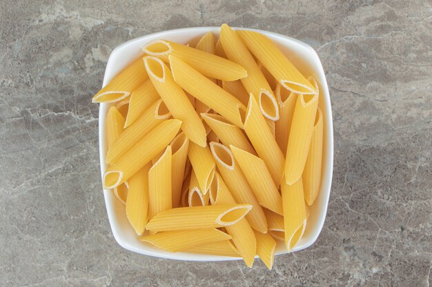 Uncooked penne pasta in white bowl.