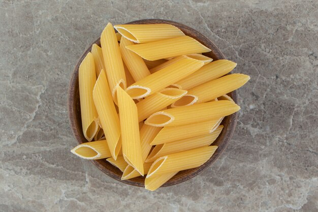 Uncooked penne pasta in wooden bowl.