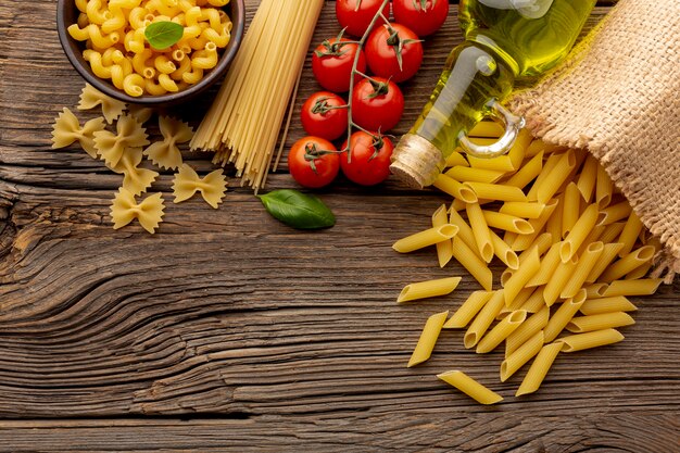 Uncooked penne spaghetti farfalle  tomatoes and olive oil on wooden table with copy space