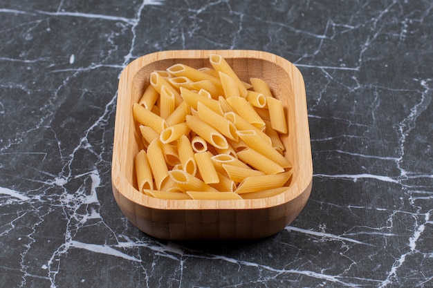 Penne di pasta cruda cruda in ciotola di legno.