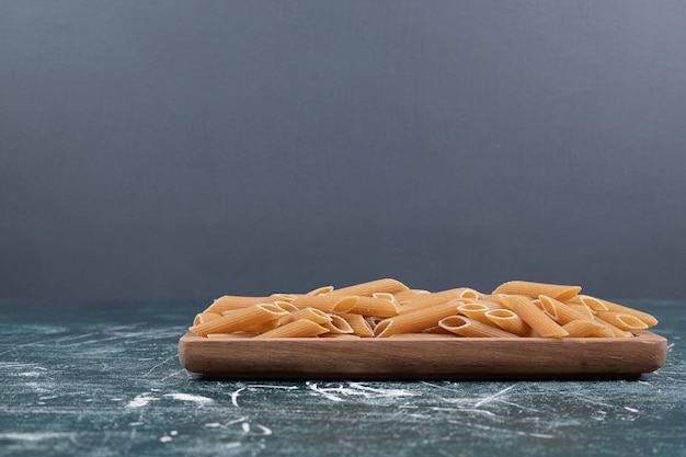 Uncooked raw penne pasta on wooden plate. High quality photo
