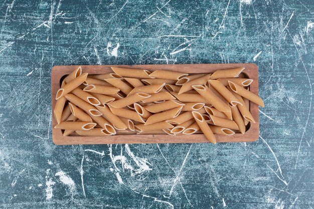 Uncooked raw penne pasta on wooden plate. High quality photo