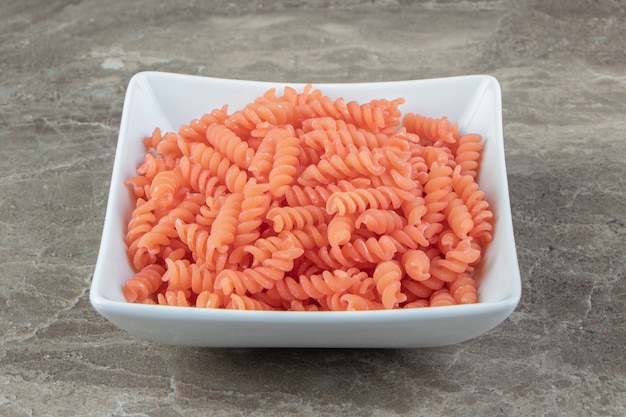 Uncooked red fusilli in white bowl