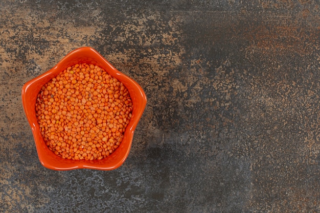 Uncooked red lentils in orange bowl.