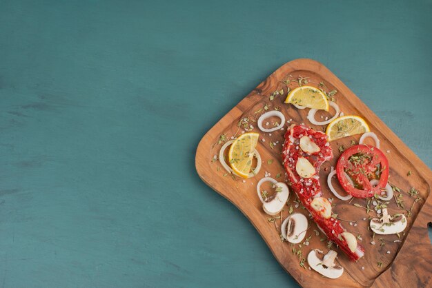 Uncooked rib meat piece with vegetables on blue table.