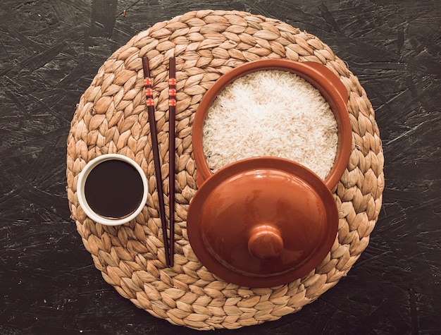 Uncooked rice grains bowl with soya sauce and chopsticks on placemat