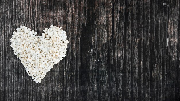 Uncooked rice made with heart on black wooden textured background