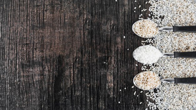 Uncooked rice in spoon over the black wooden backdrop