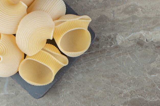 Uncooked seashell pasta on black plate