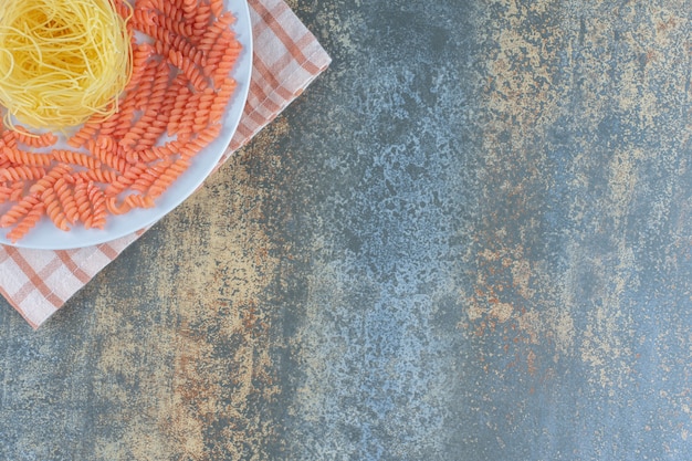 Foto gratuita spaghetti crudi e fusilli in una ciotola sul tovagliolo, sullo sfondo di marmo.