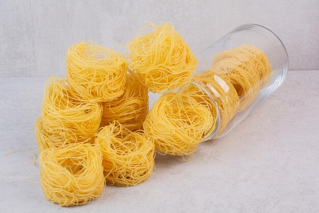 Uncooked spaghetti nests on marble table with jar.