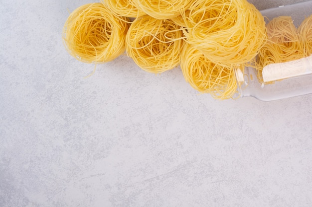 Foto gratuita nidi di spaghetti crudi sulla superficie di pietra con vaso di vetro