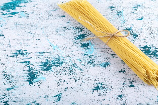 Uncooked spaghetti pasta tied with rope on colorful surface.