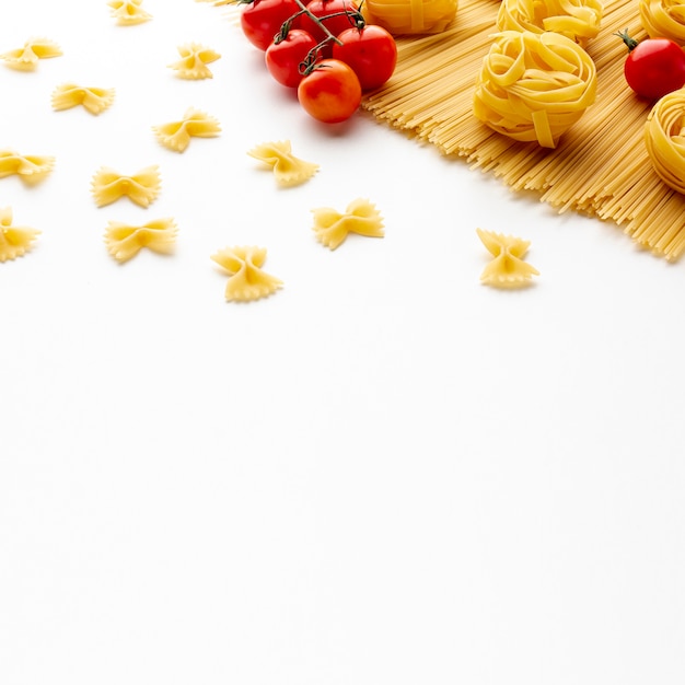 Uncooked spaghetti tagliatelle farfalle and tomatoes with copy space