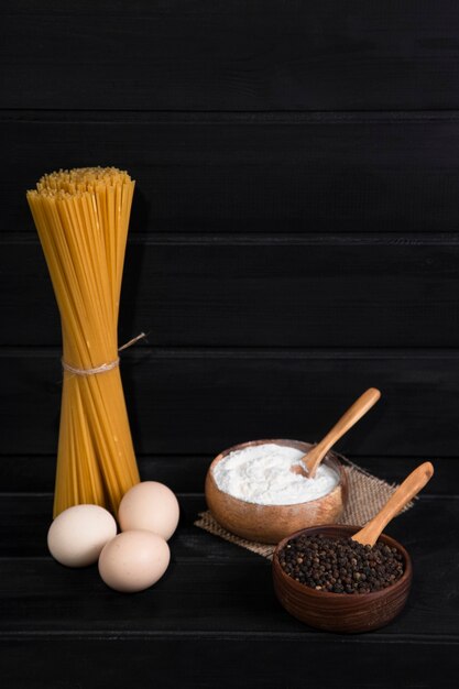 Uncooked spaghetti tied with rope and peppercorns placed on a wooden table . High quality photo