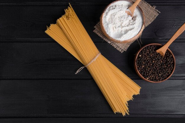 Uncooked spaghetti tied with rope and peppercorns placed on a wooden table . High quality photo