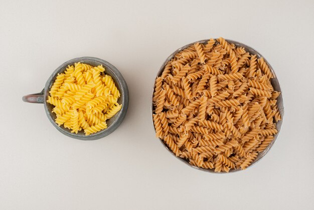 Uncooked spiral macaroni in cup and bowl