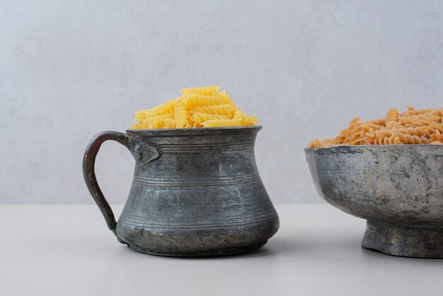 Uncooked spiral macaroni in cup and bowl.