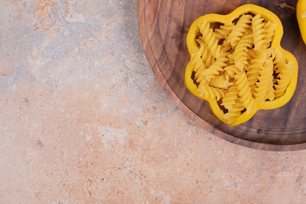 Uncooked spiral macaroni with pepper on wooden board