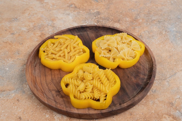 Uncooked spiral macaroni with pepper on wooden board