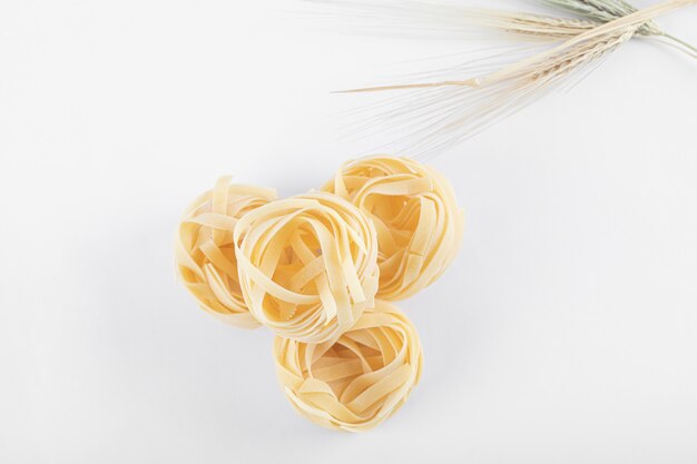 Uncooked tagliatelle nests on white.