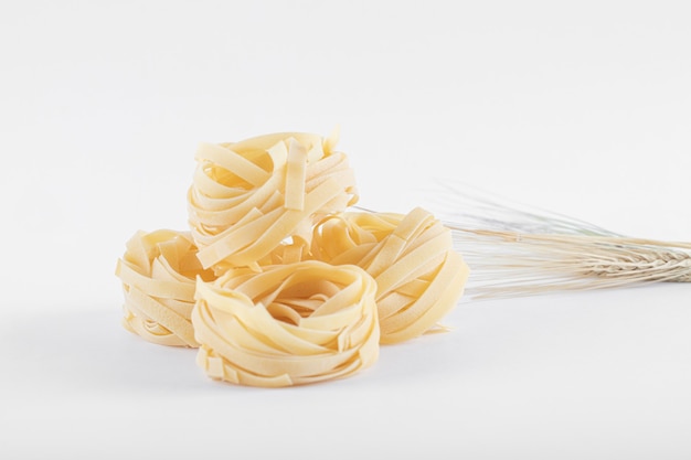 Uncooked tagliatelle nests on white.