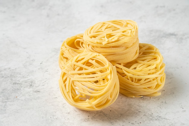 Uncooked tagliatelle pasta nests on white background. 
