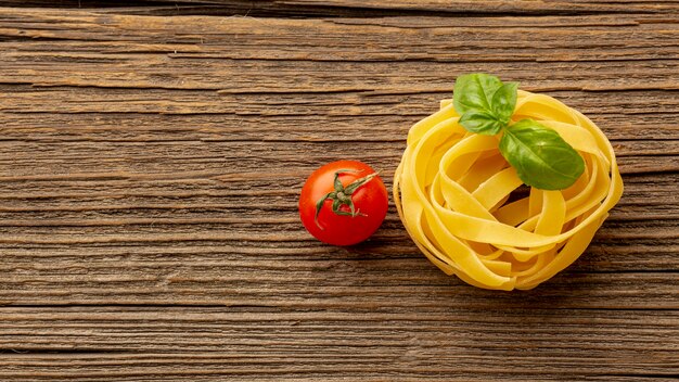 Uncooked tagliatelle with basil leaves and tomatoes