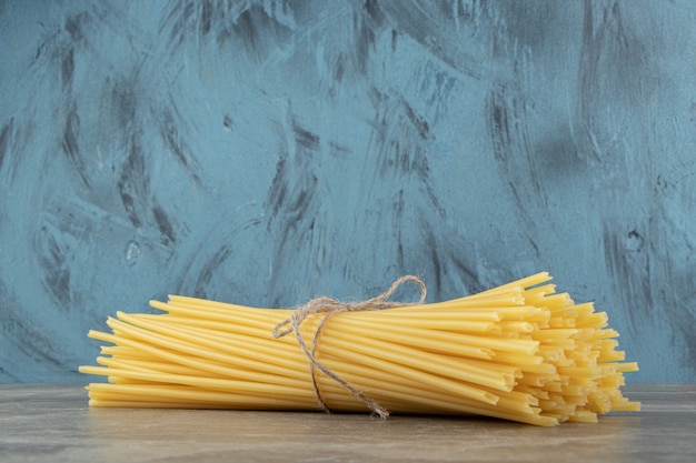 Uncooked tube spaghetti tied with rope on marble surface