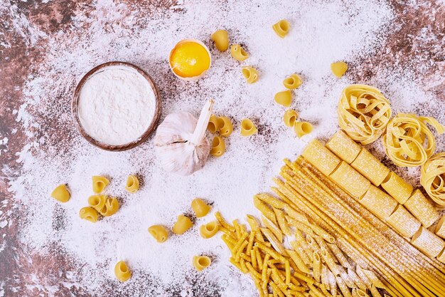 Uncooked various pasta with flour on wooden table. 