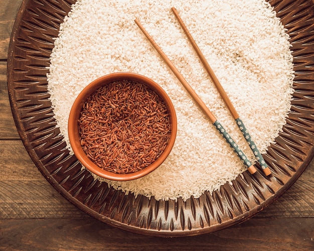 Uncooked white and red jasmine rice grains with chopsticks on wooden tray