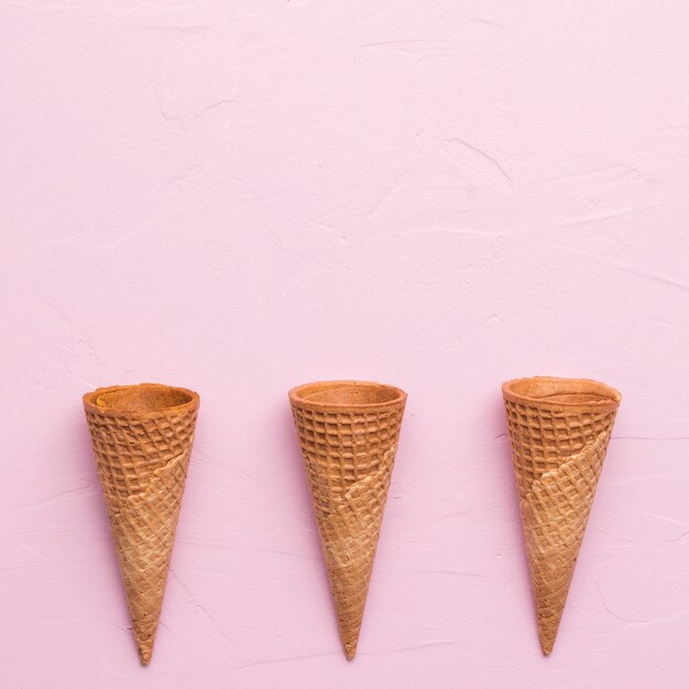 Unfilled waffle ice cream cones on pink surface