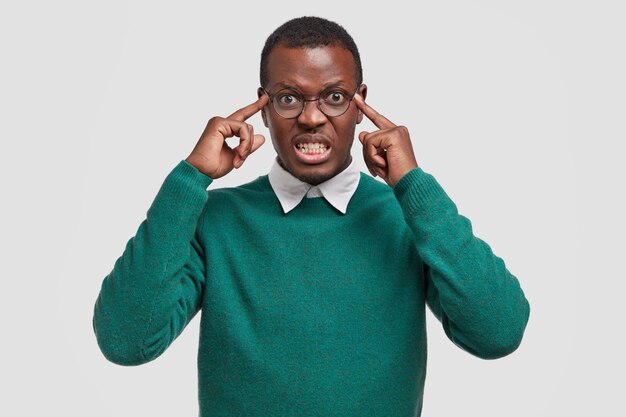 Unfocused displeased bothered African American man adult holds fingers on temples, tries to concentrate, has terrible headache, clenches teeth