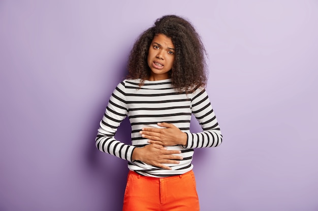 Free photo unhappy afro american woman touches belly, suffers from menstrual period cramp