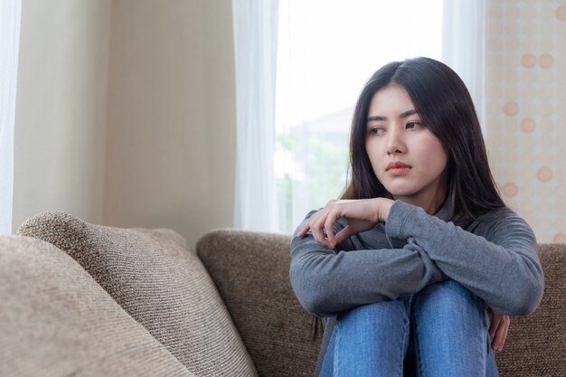 Free photo unhappy asian pretty young woman siting alone on couch with feeling sadness