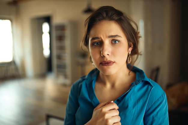 Unhappy attractive young woman in blue shirt having mournful sorry facial expression.