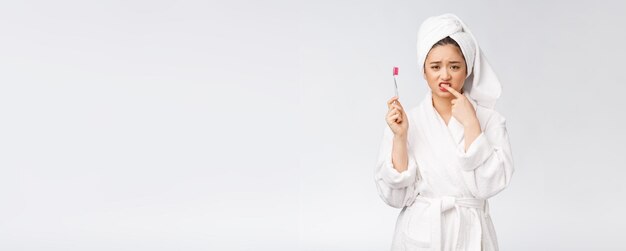 Unhappy beautiful woman brushing her teeth on white background