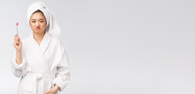 Unhappy beautiful woman brushing her teeth on white background