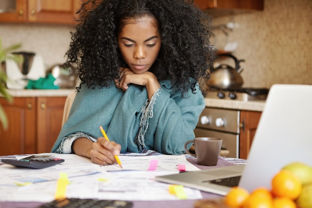 Unhappy depressed young dark-skinned housewife managing domestic budget alone at night