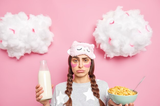 Unhappy displeased brunette woman with hydrogel patches under eyes has unhappy look dressed in pajama