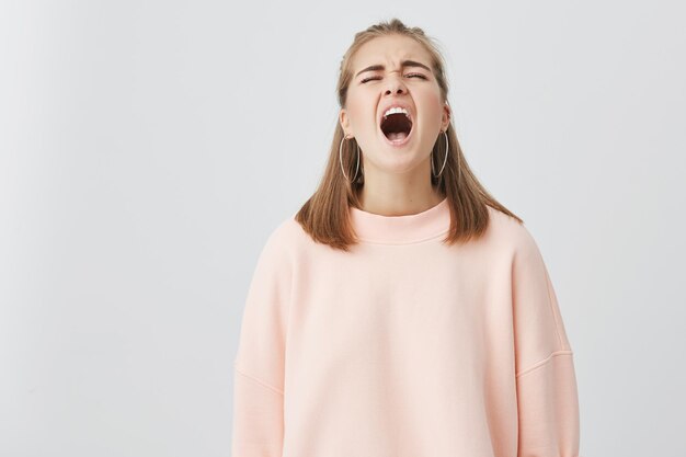 Unhappy emotional young screaming in despair and crying girl , opening mouth widely, shocked with bad news, standing isolated against gray studio wall