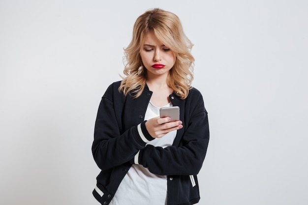 Giovane donna accigliata infelice che per mezzo dello smartphone